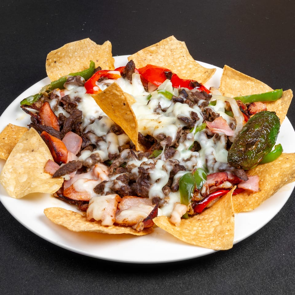 Loaded plate of tortilla chips topped with melted cheese, seasoned beef, grilled peppers, onions, and roasted jalapeño.