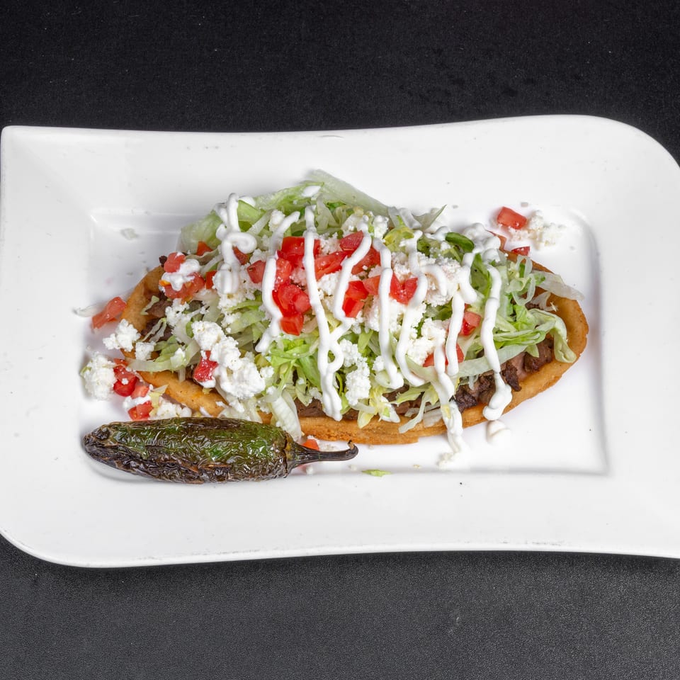 Crispy Mexican-style flatbread topped with lettuce, tomatoes, crumbled cheese, and cream sauce, served with a roasted pepper.