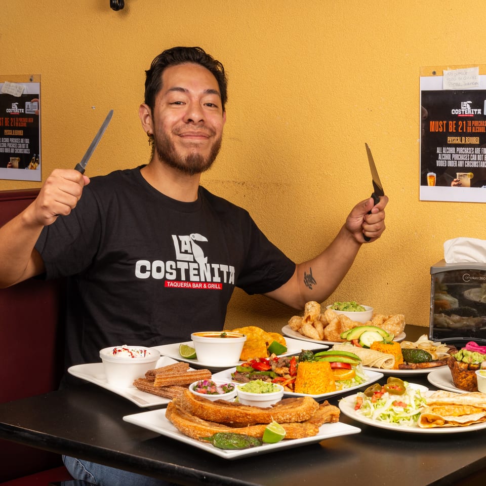 Restaurant staff member poses with knives behind a table filled with tacos, chicharrones, churros, rice, guacamole, and other Mexican dishes.