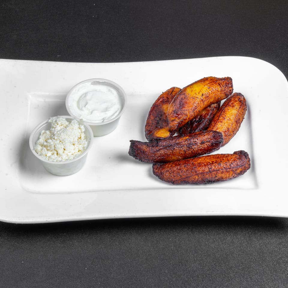 Fried plantains served on a white platter with small bowls of creamy sauce and crumbled cheese.