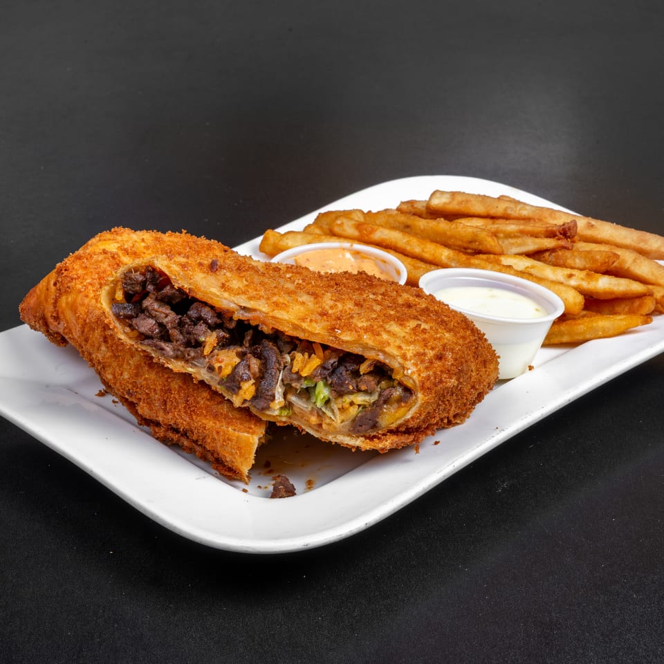 Crispy stuffed pastry filled with beef, beans, rice, and vegetables, served with fries and dipping sauces on a white plate.