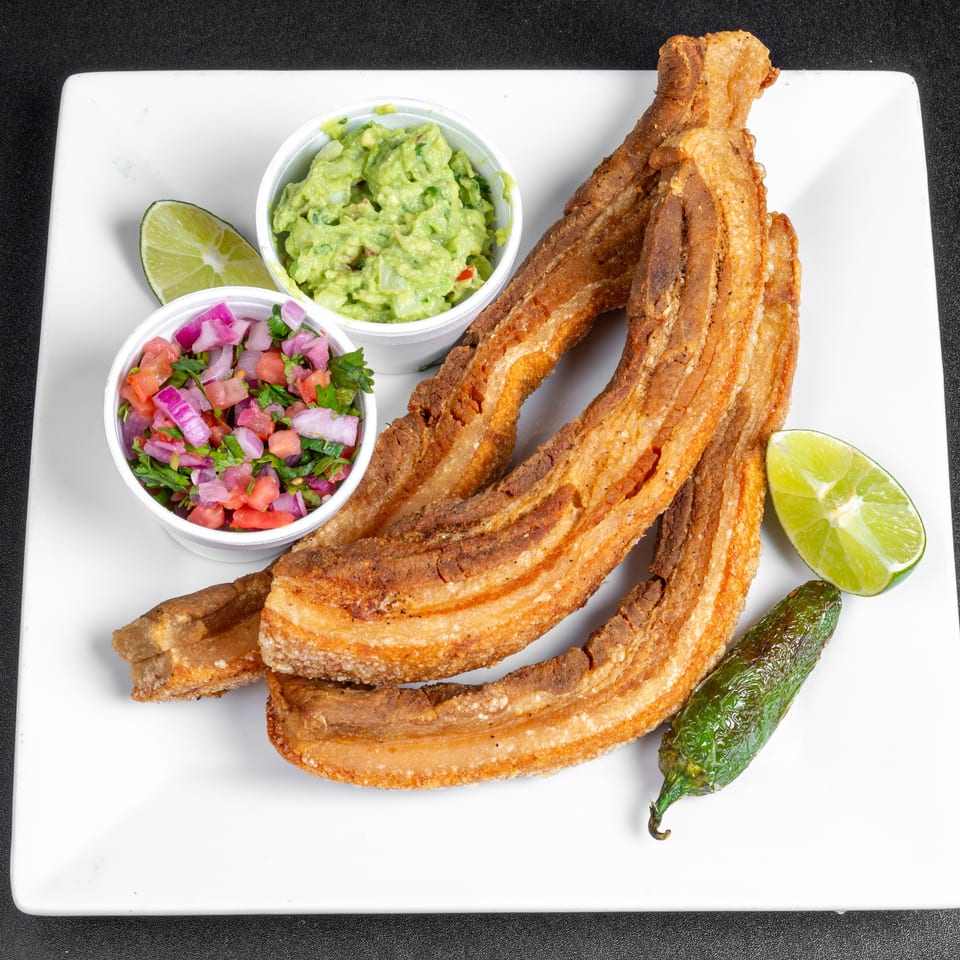 Crispy fried pork belly strips served with guacamole, pico de gallo, lime wedges, and a roasted green chile.