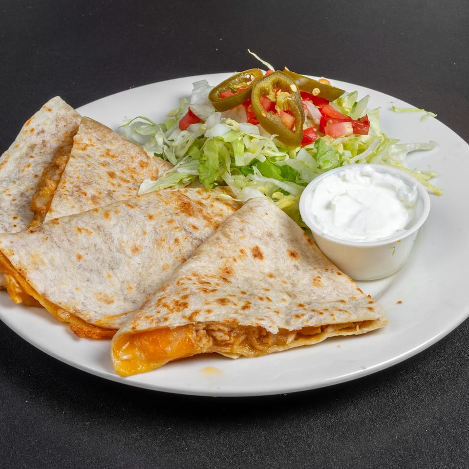 Cheesy quesadilla wedges served with shredded lettuce, diced tomatoes, jalapeños, and sour cream on a white plate.
