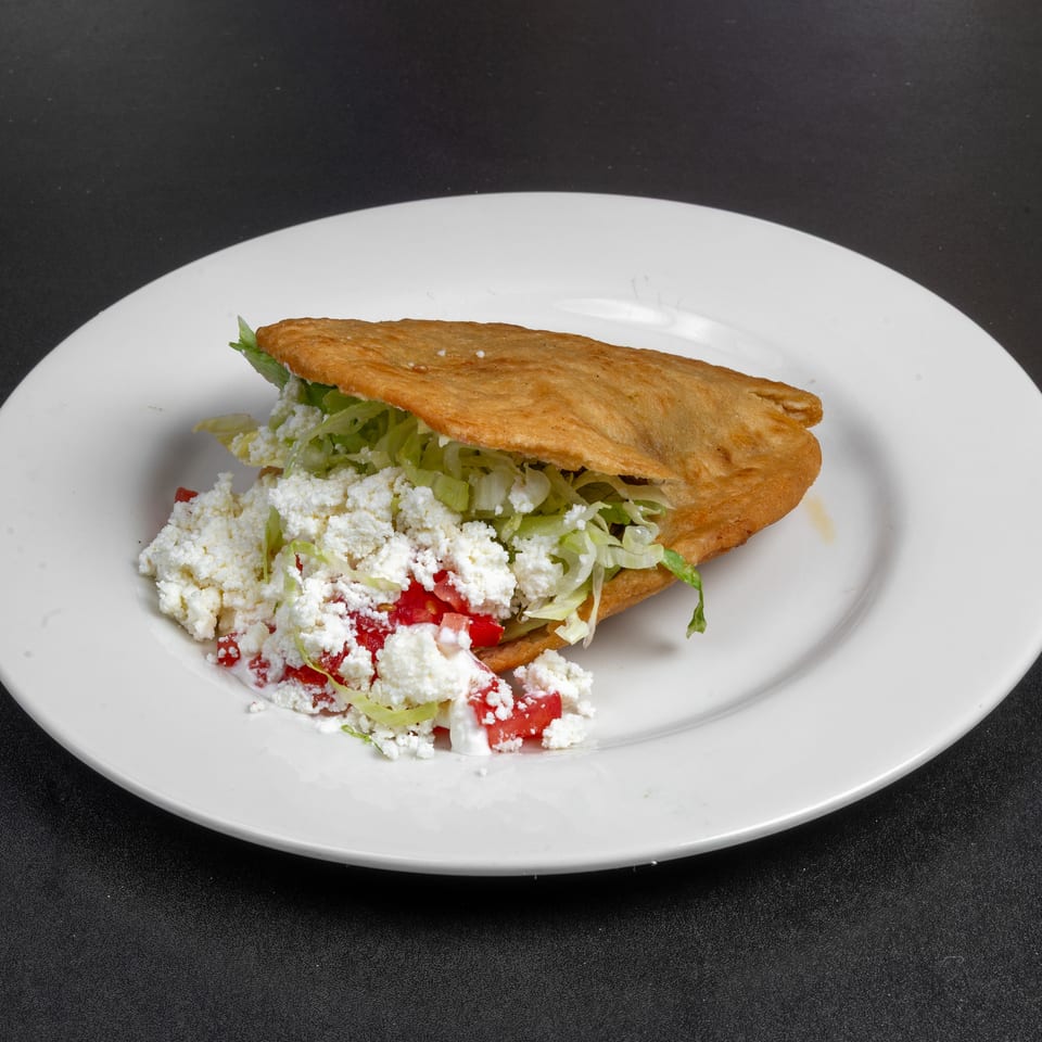 Crispy folded taco filled with lettuce, tomatoes, and crumbled white cheese on a white plate.