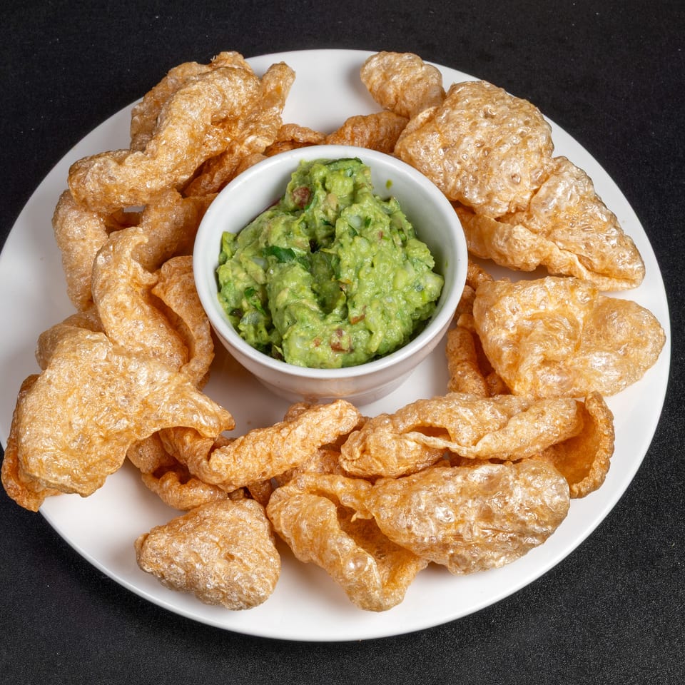 Crispy golden tortilla chips surround a bowl of chunky guacamole on a white plate against a black background.